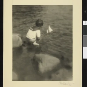 Photograph by Olaf Christoffersen of a child playing with a sailboat on a calm water surface, evoking tranquility and the simplicity of childhood.