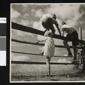 Photograph by Olaf Christoffersen of two boys standing on a fence in Asker, with a younger girl looking up, capturing childhood's mix of courage and longing.