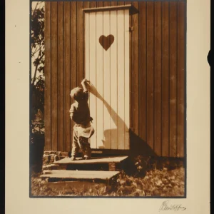 Child reaching for the doorknob on an outhouse door with a heart-shaped cutout in Asker.