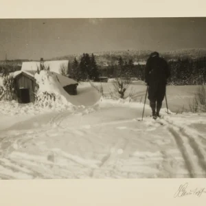 Winter landscape photographed by Olaf Christoffersen, showing a solitary skier on a snowy path, with a snow-covered cabin and trees in the background, evoking peace and quiet.