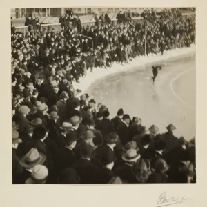 Photograph by Olaf Christoffersen of a speed skater in action at Frogner Stadium, 1920s, with a lively crowd of spectators in the background, capturing the energy of the event.