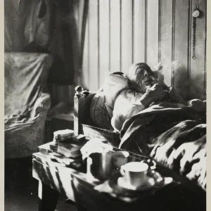 Photograph by Olaf Christoffersen of an elderly man resting in bed at home in Asker, smoking a pipe, evoking themes of reflection, aging, and intimacy.
