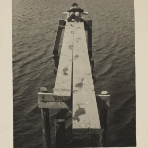 Photograph by Olaf Christoffersen of a child resting on an old pier, with wet footprints leading across the planks, evoking the calm and joy of a summer day.