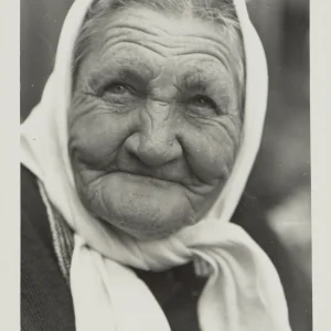 Photograph by Olaf Christoffersen of an elderly woman wearing a headscarf, her face etched with deep wrinkles and a warm smile, embodying a life of experiences.